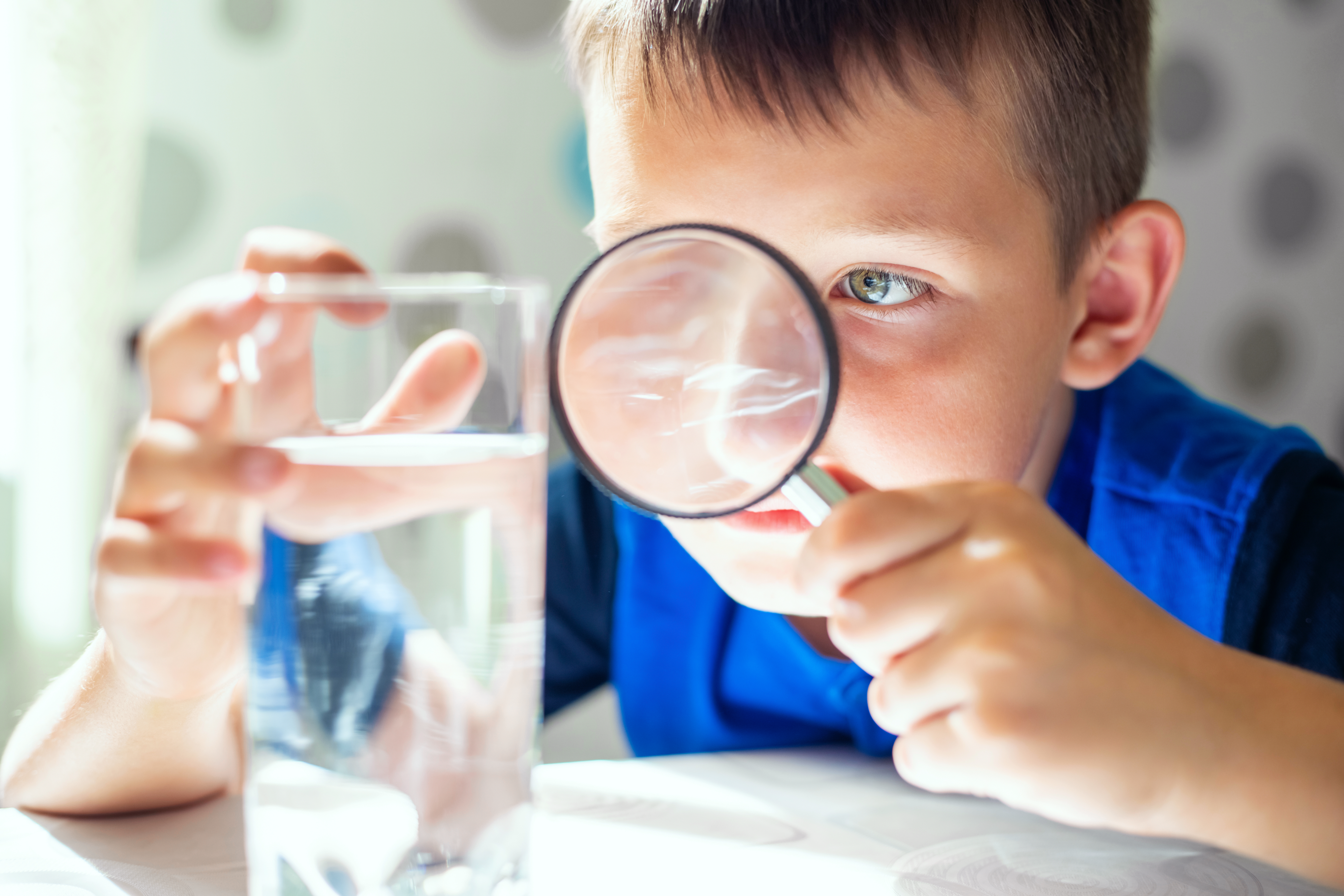 Kind hält Lupe vor ein Wasserglas