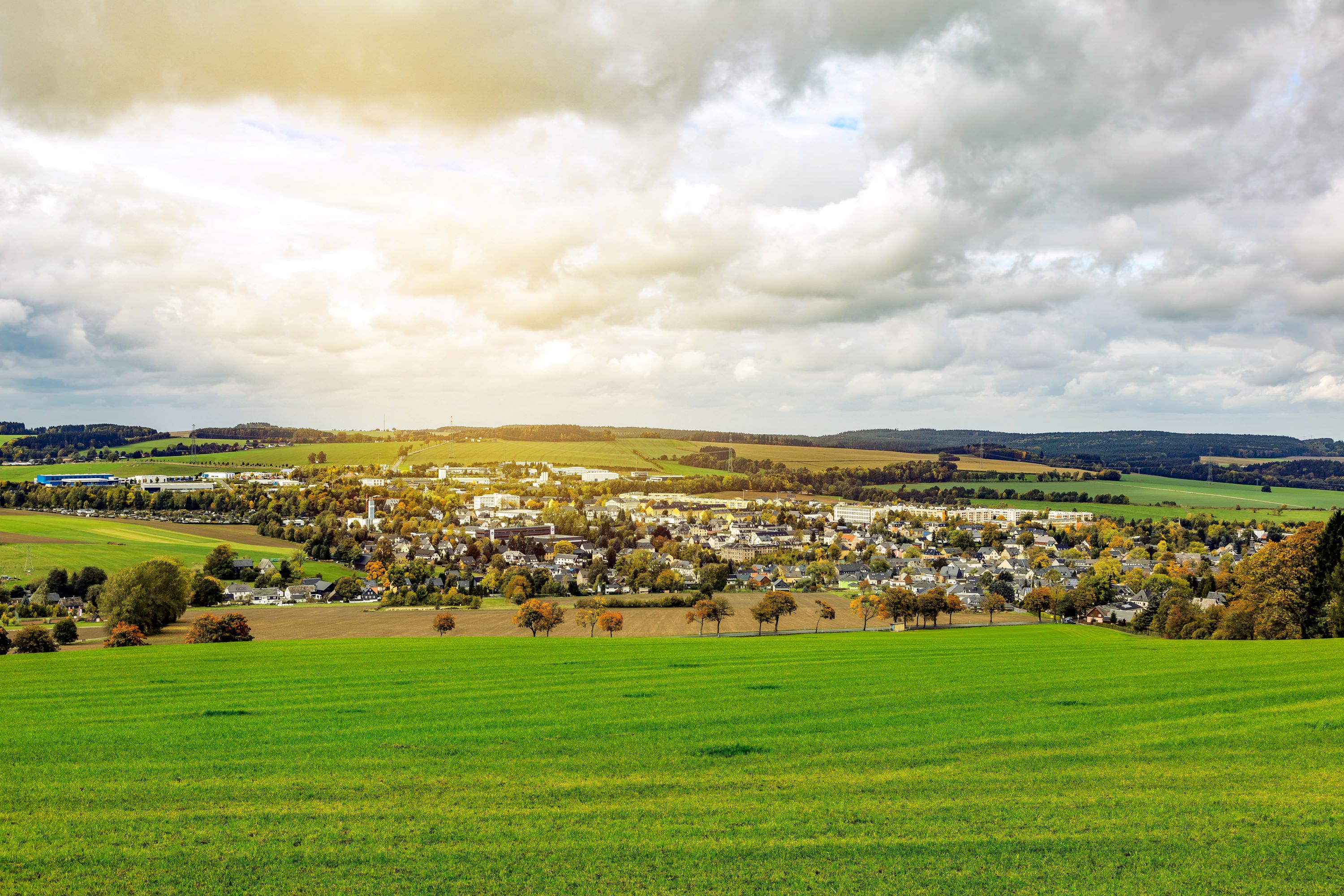 Zwönitz inmitten grüner Felder und Hügel unter bewölktem Himmel.