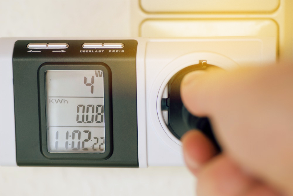 Hand steckt Stecker in eine Steckdose mit Messgerät daneben