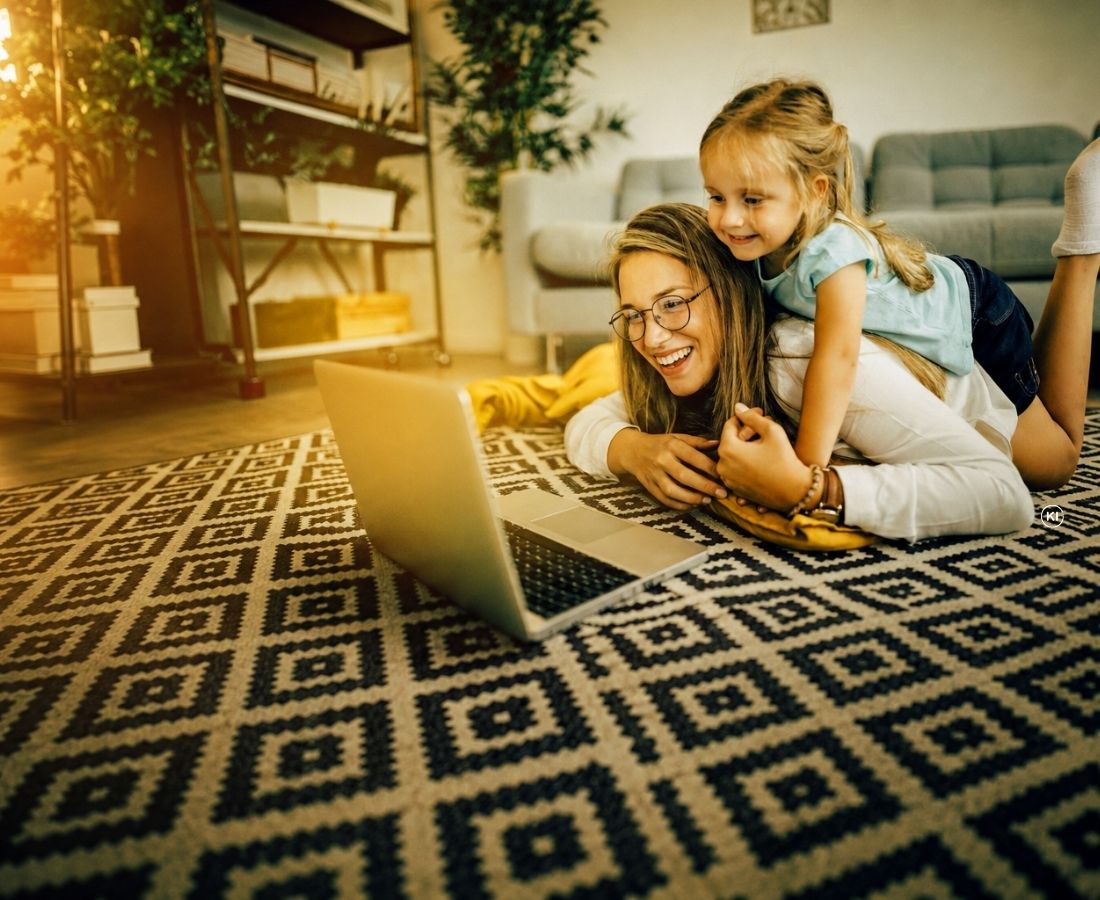 Mutter und Kind liegen auf dem Fußboden und schauen auf den Laptopbildschirm.