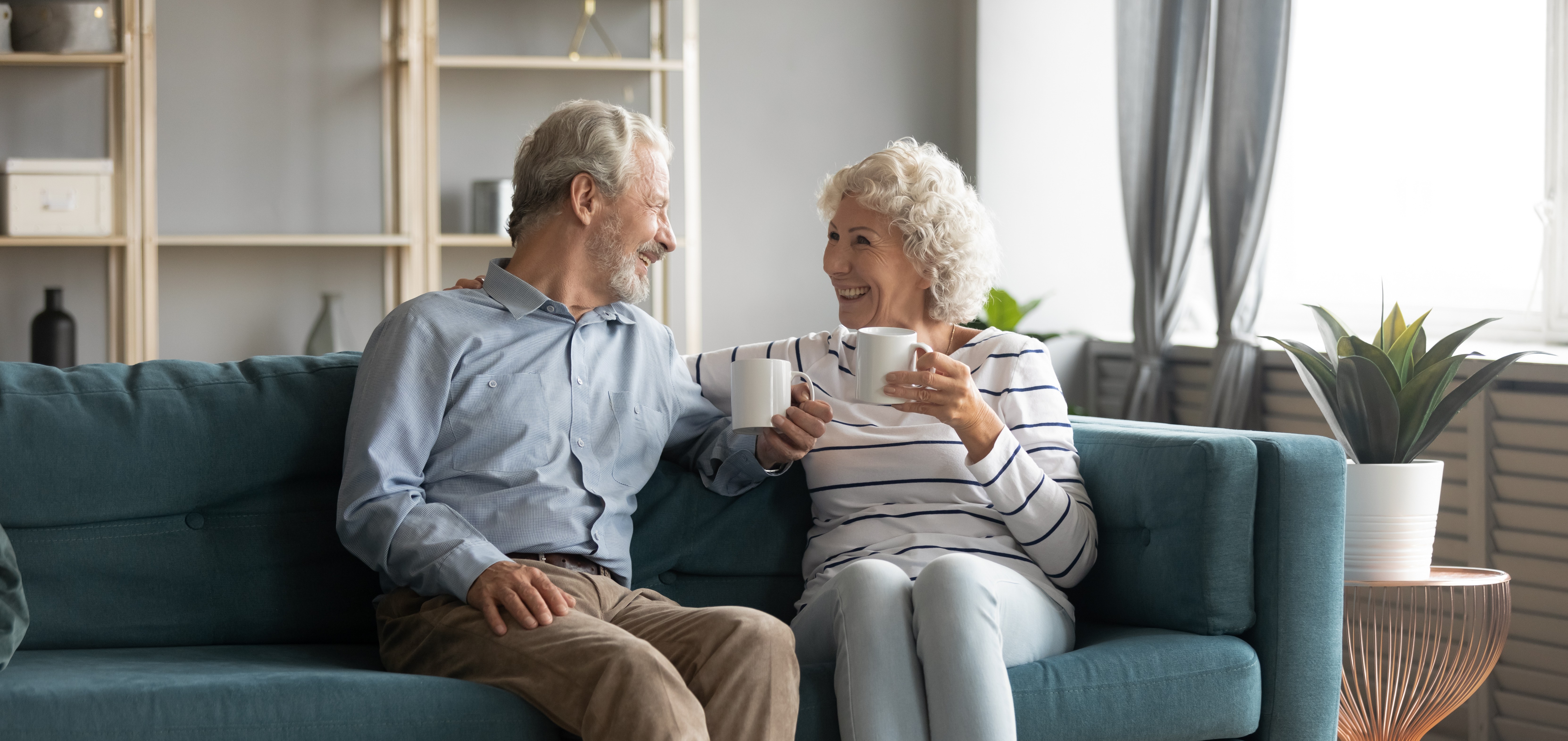 Ein Rentner-Ehepar sitzt Kaffetrinkend auf einer Couch