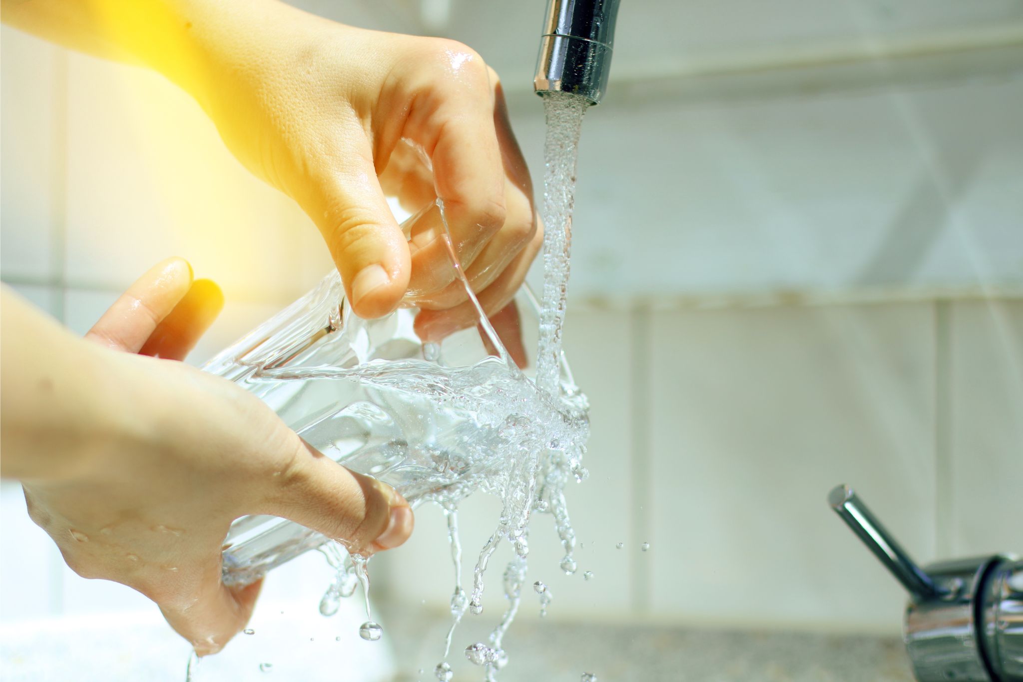 zwei Hände halten ein Wasserglas unter einen laufenden Wasserhahn