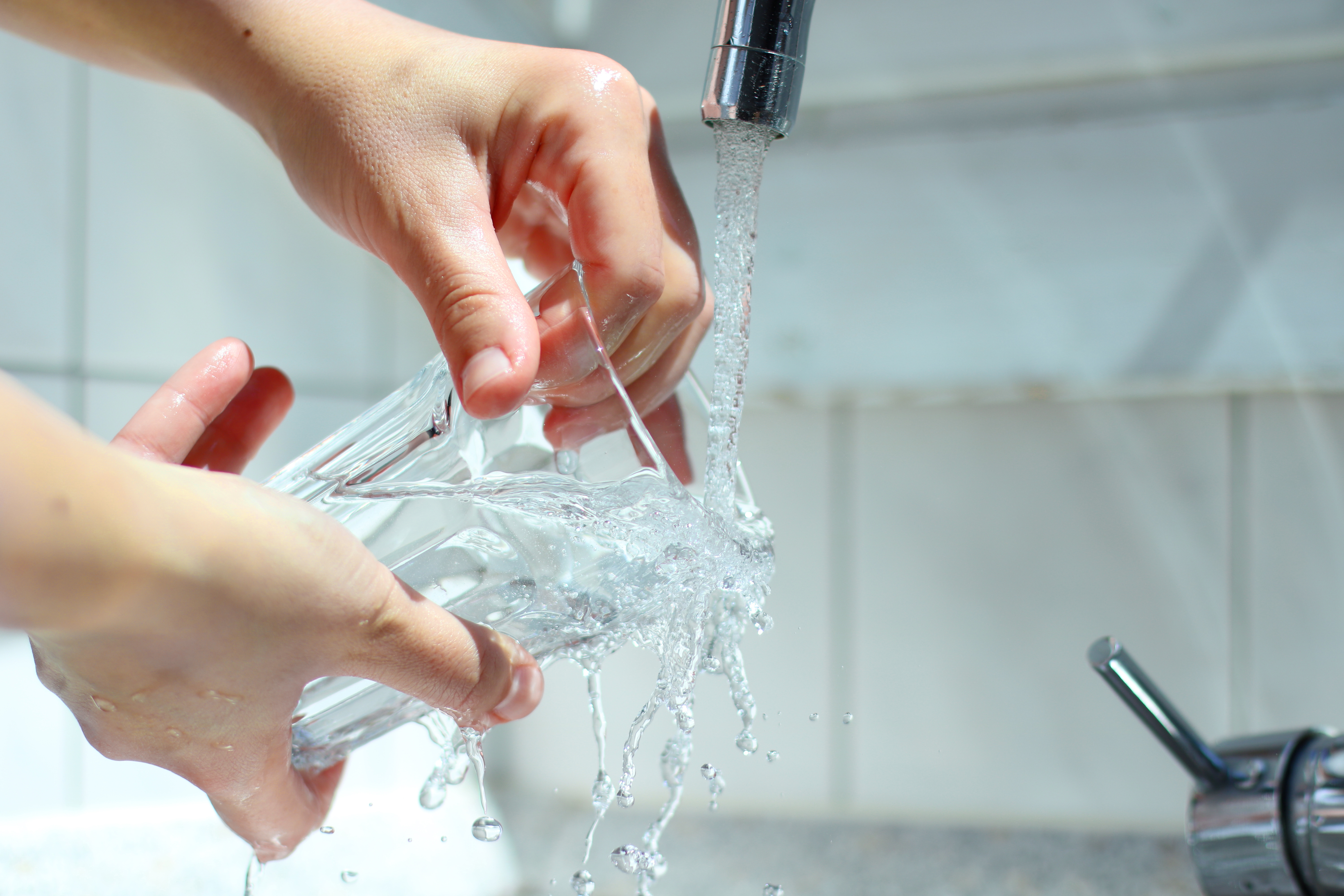 zwei Hände halten ein Wasserglas unter einen laufenden Wasserhahn