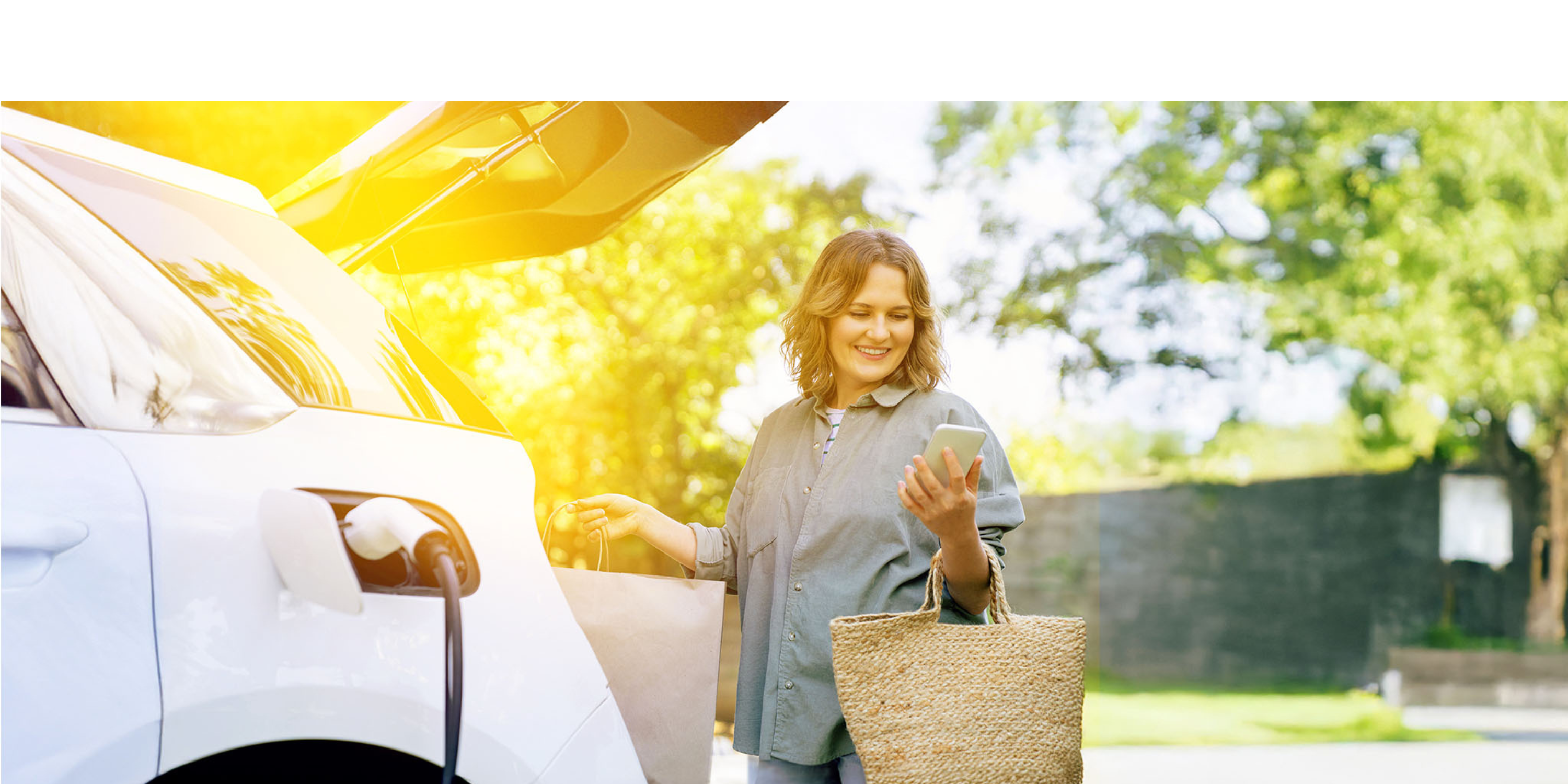 Eine Frau lädt ihre Einkäufe in den Kofferraum während ihr Elektroauto lädt.