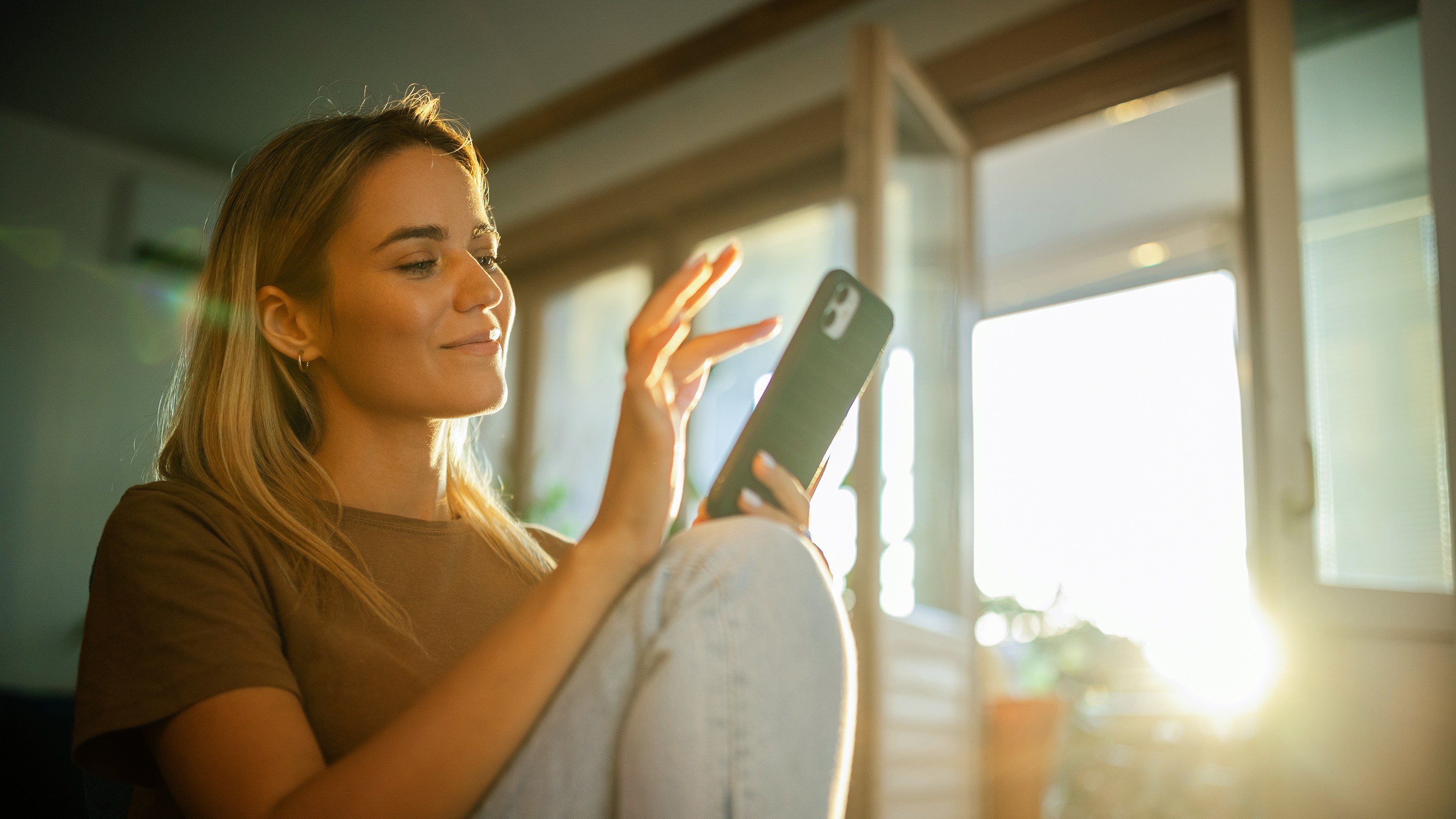 Junge Frau sitzt gemütlich mit dem Handy auf dem Sofa.