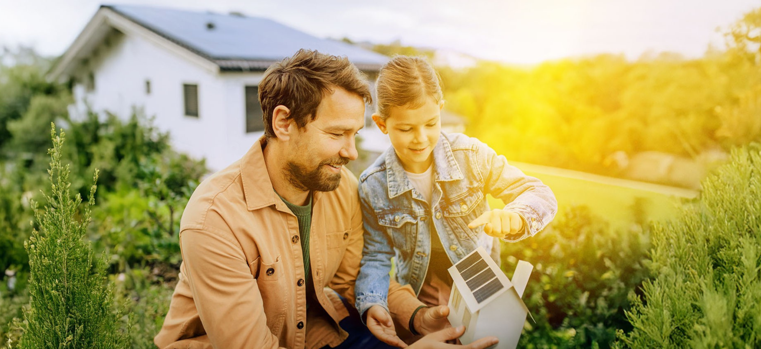 Papa erklärt Tochter Solar im Garten anhand eines Papphauses
