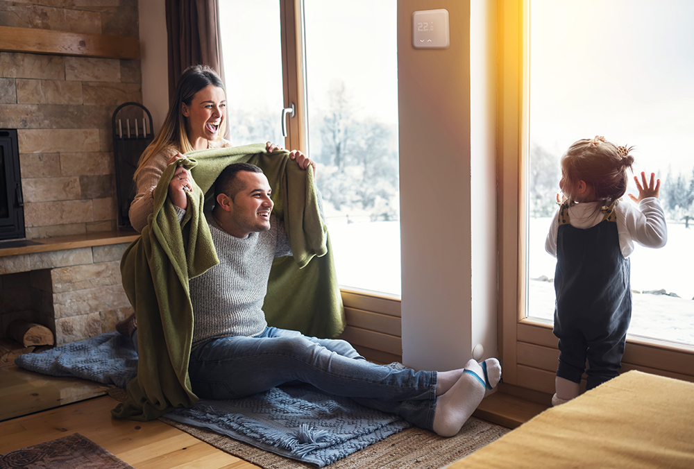 Familie sitzt vor Bodentiefen Fenstern, draußen liegt Schnee