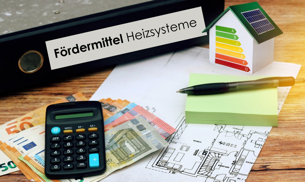 Euro-Geldscheine, Taschenrechner, Bauplan und Aktenordner mit dem Text "Fördermittel Heizsysteme" liegen auf einem Holztisch