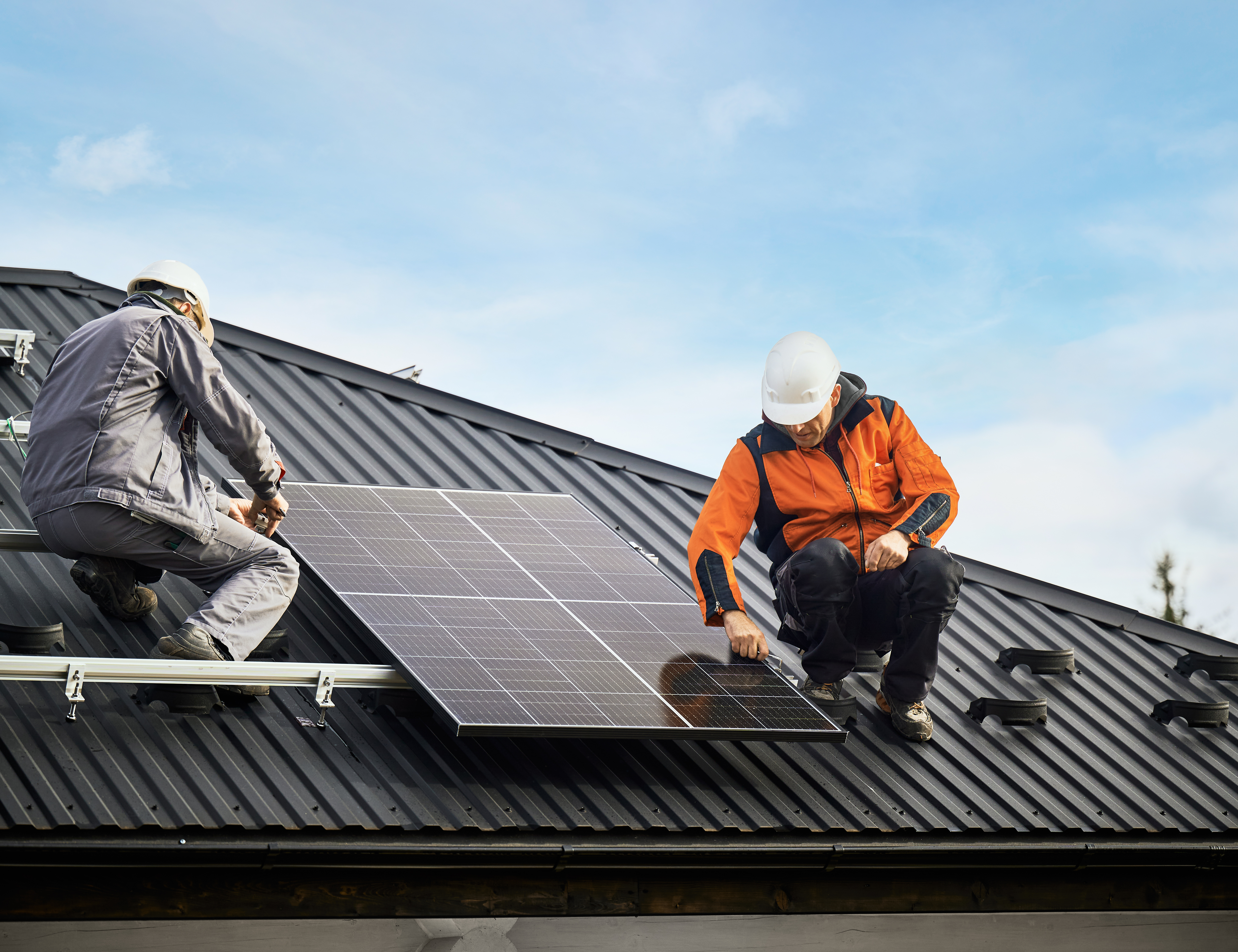 Zwei Handwerker sind auf einem Gebäudedach und montieren ein Solarpanel 