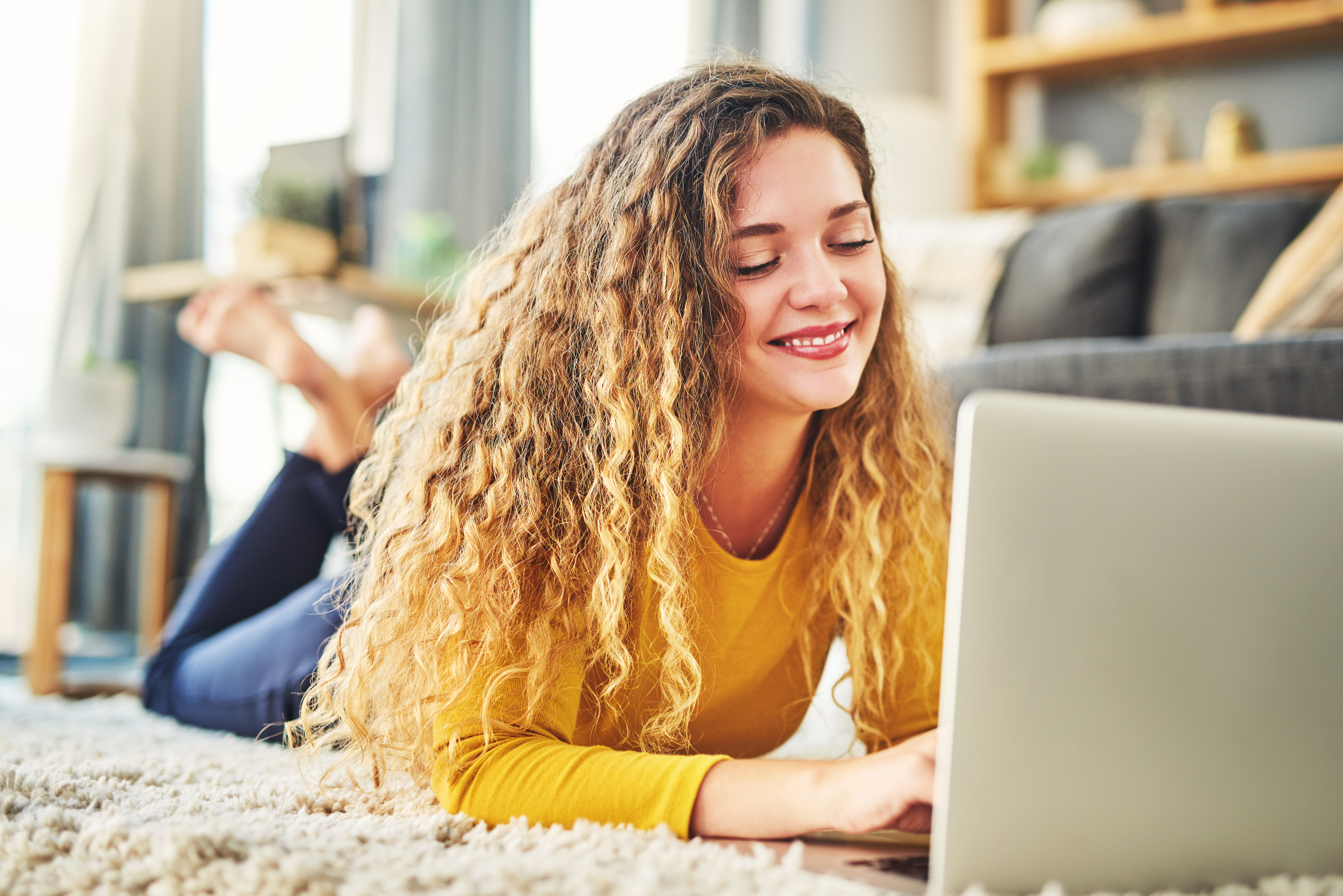 Frau in gelben Top liegt auf dem Boden vor einem Laptop