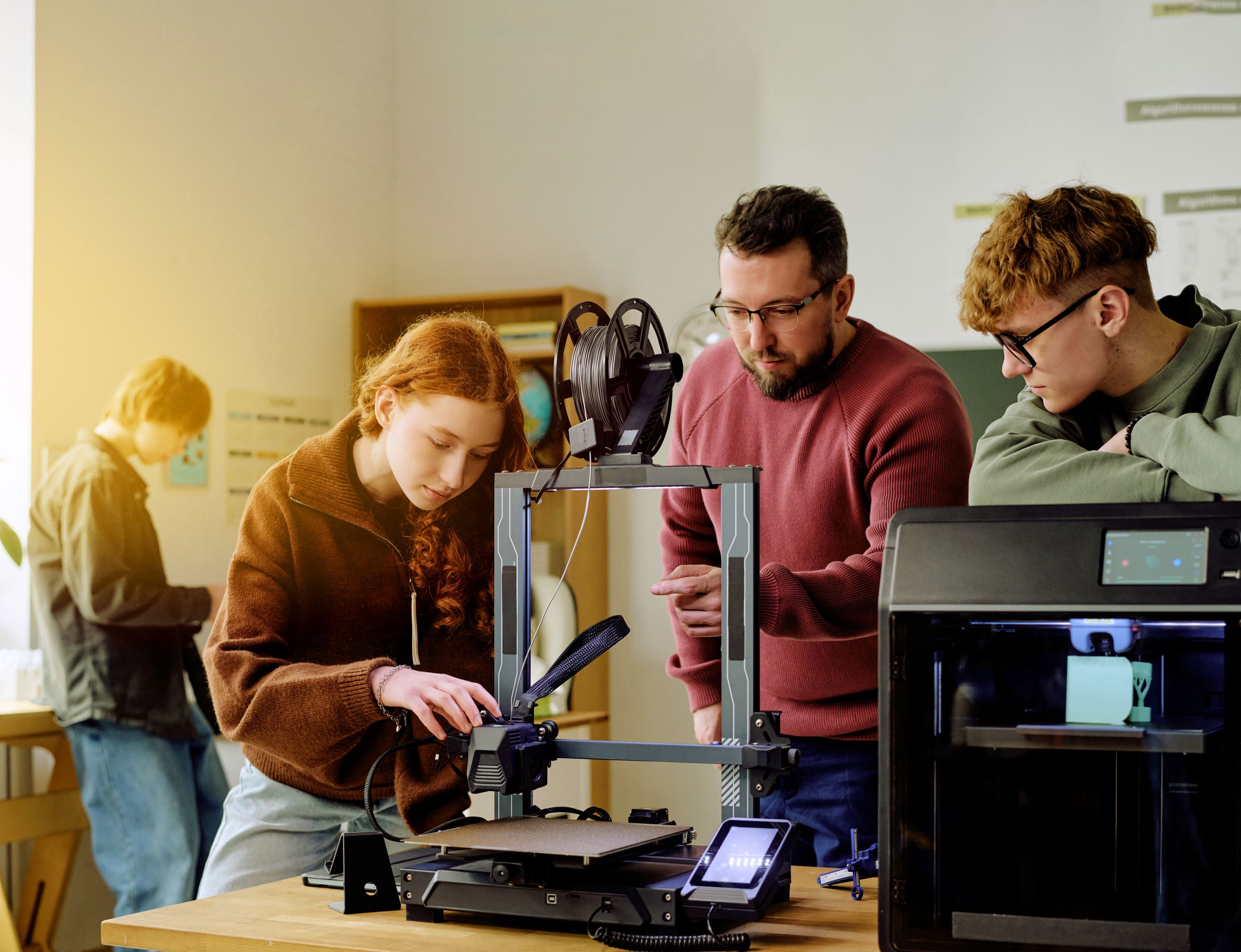 Gruppe junger Menschen nutzt 3D-Drucker in einem modernen Lernumfeld.