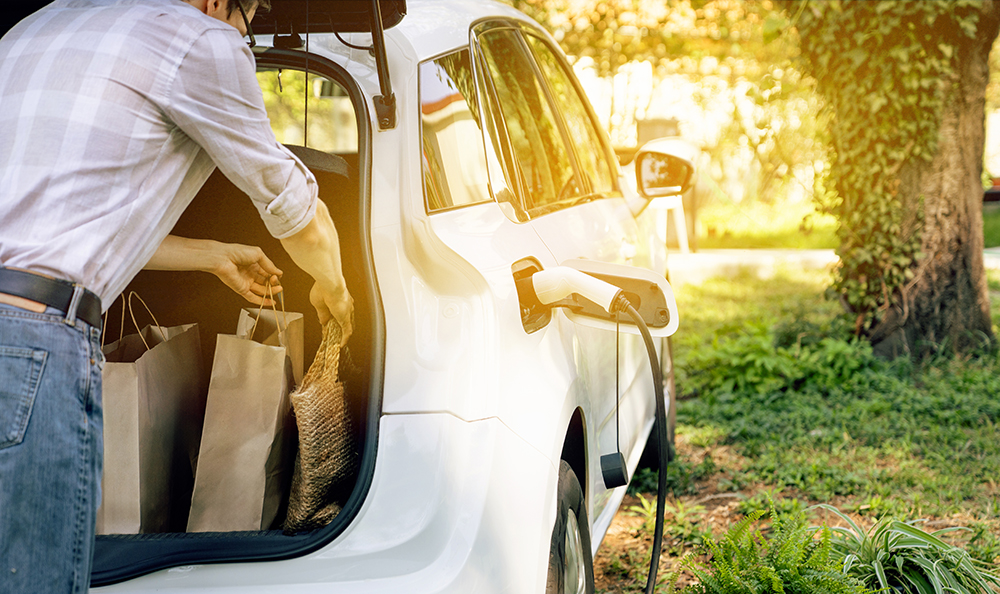 Mann holt aus dem Kofferraum seine Einkäufe raus, während das Fahrzeug an der Wallbox Strom tankt
