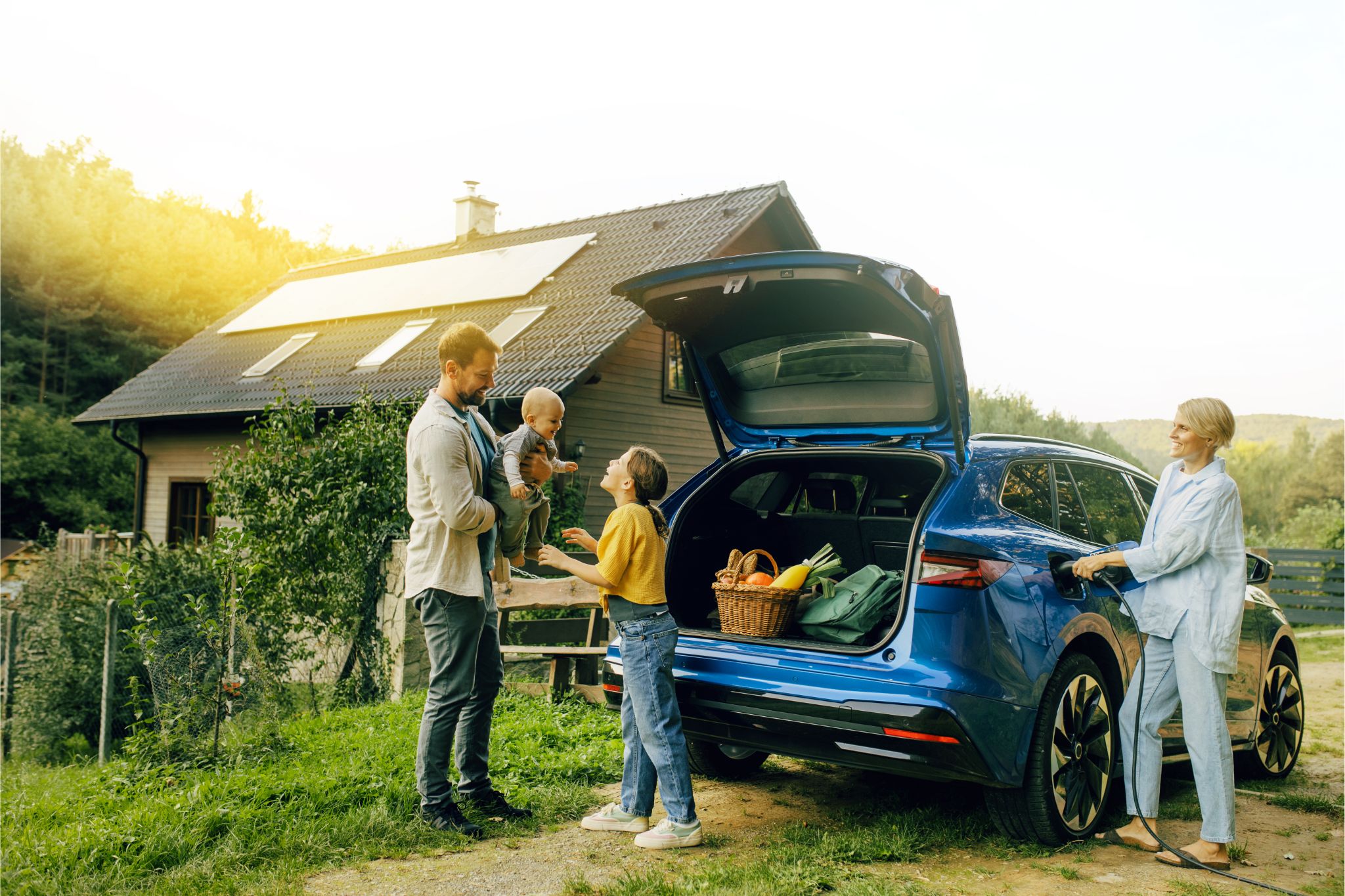 Eine Familie steht vor ihrem Einfamilienhaus mit Solar auf dem Dach und ihrem Elektroauto davor