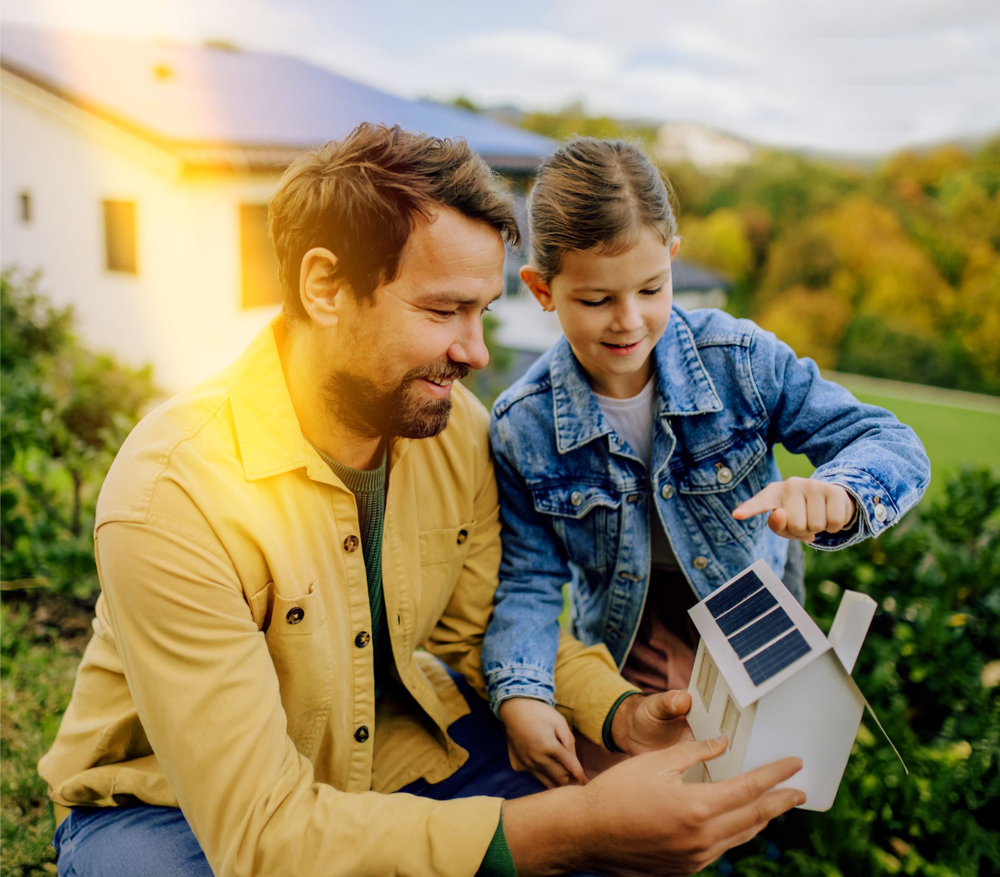 Kleine Tochter mit ihrem Vater der ein Papierhaus mit Solarpanelen hält
