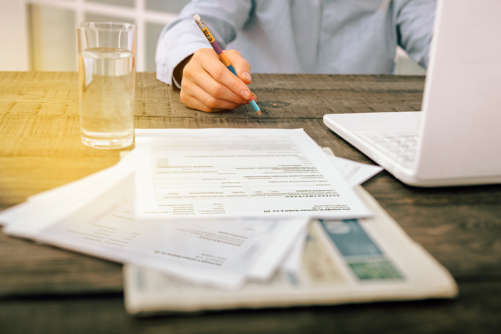 Mann in Hemd sitzt vor Laptop auf einem Tisch und hält ein eins Bleistift über Unterlagen