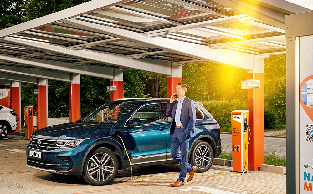 Mann telefoniert, während sein e-Auto geladen wird