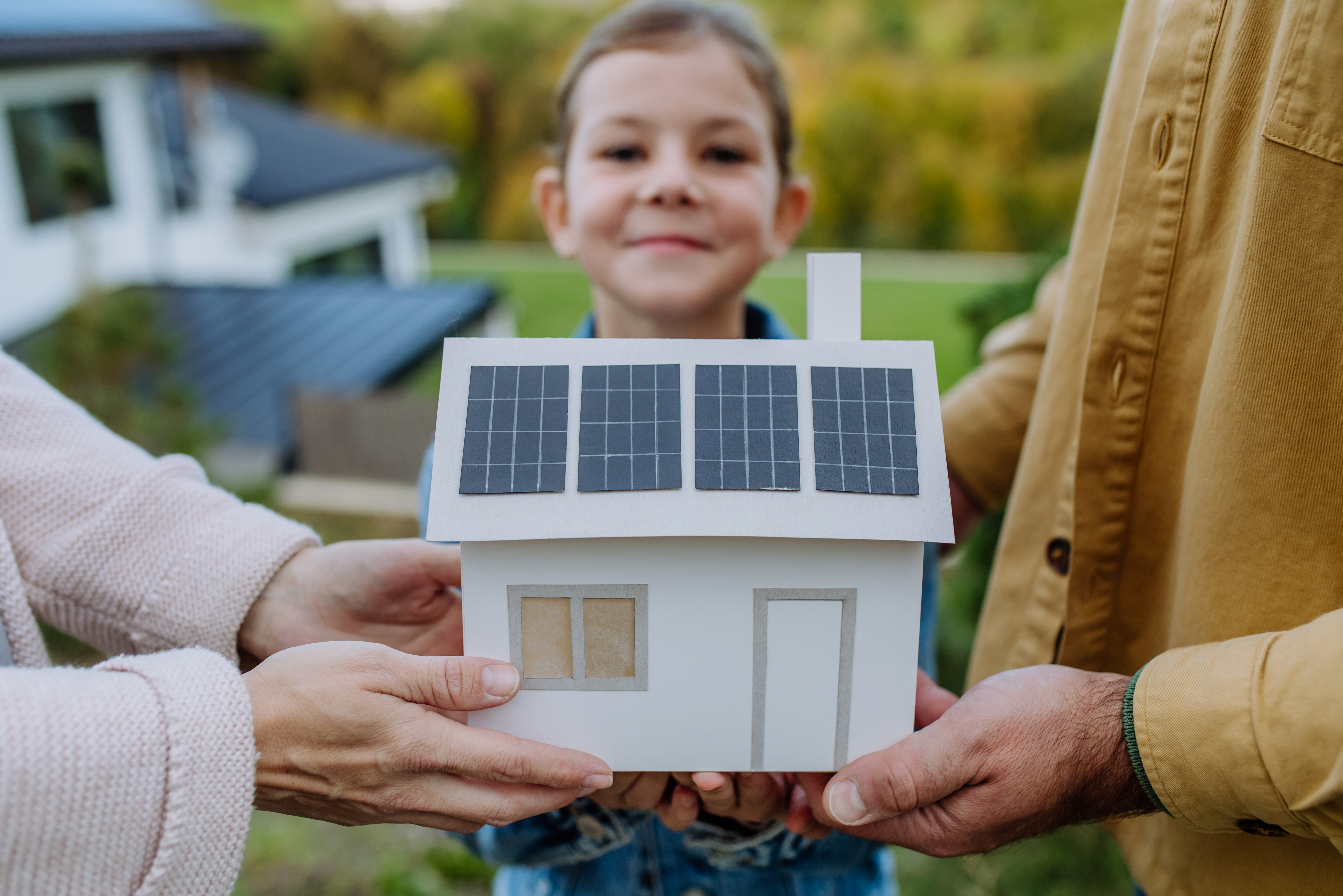 gebastelte Photovoltaikanlage auf einem Papierhaus mit Mädchen im Hintergrund