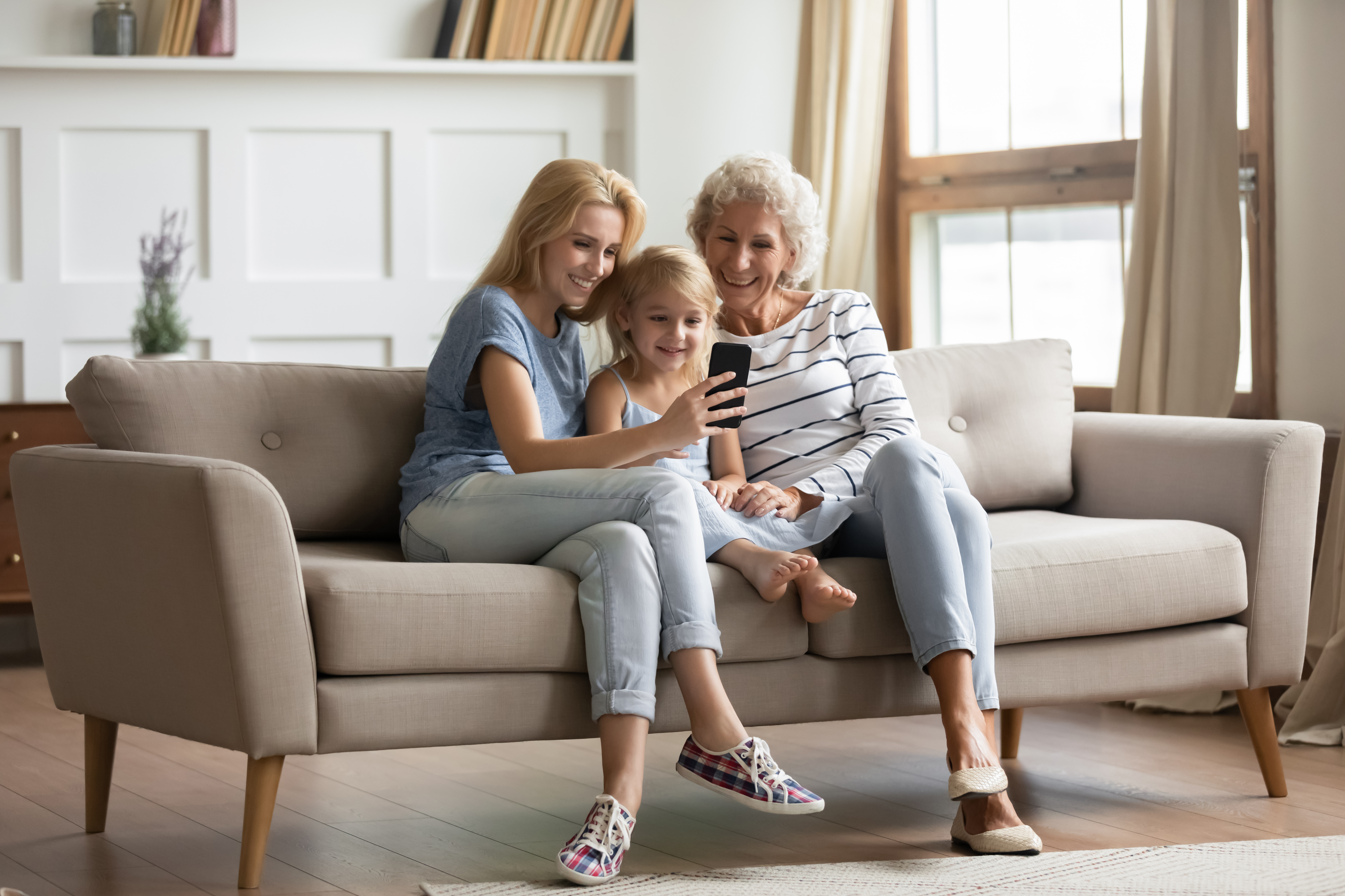 Mutter, Tochter und Enkelin sitzen auf einer Couch und betrachten ein Handy