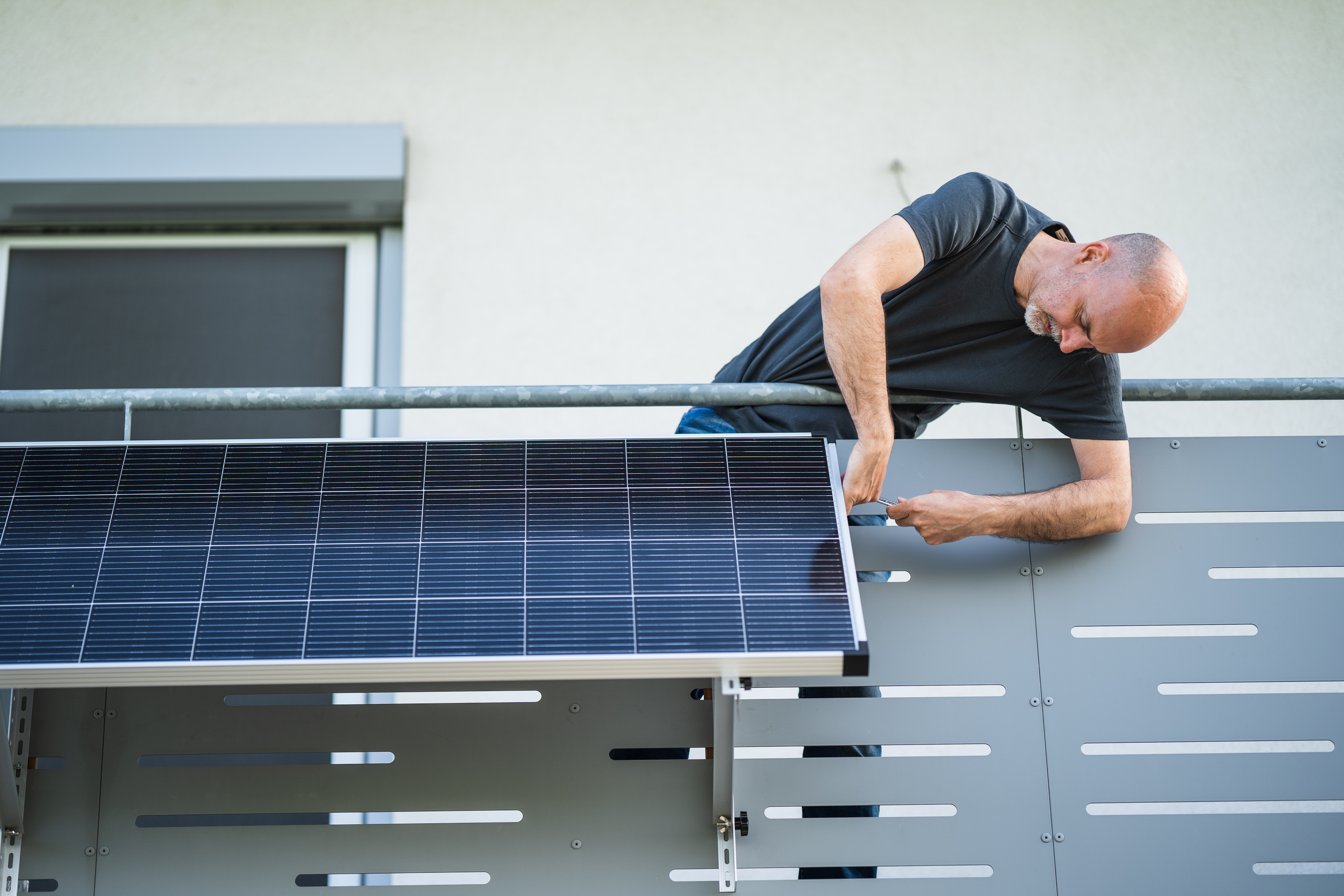 ein Mann installiert an seinem Balkongeländer ein Solarpanel