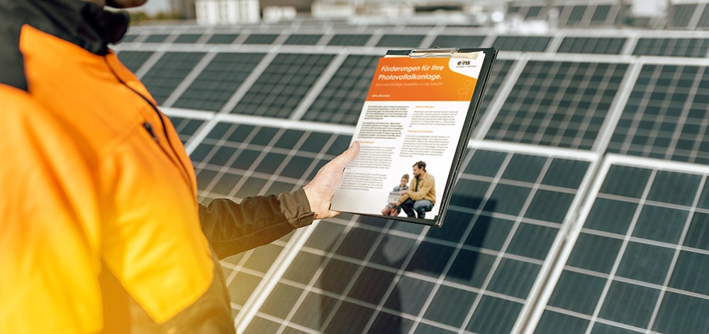 Mann in Arbeitskleidung steht vor Solarpanels und hält einen Solar-Förderantrag in der Hand