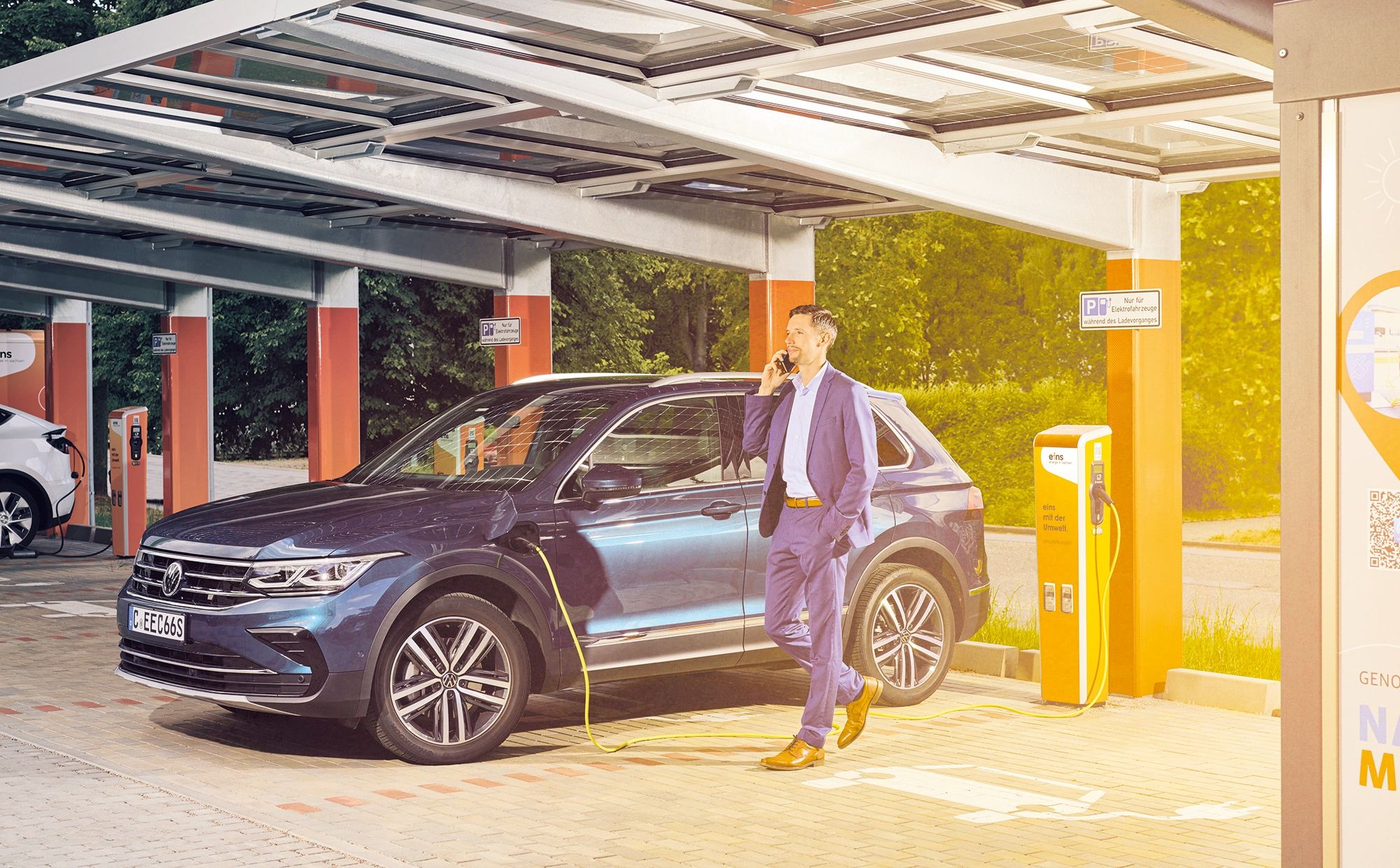 Mann telefoniert, während sein e-Auto geladen wird