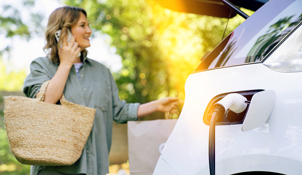 Frau steht neben ihrem Auto und telefoniert, während das Fahrzeug Strom tankt