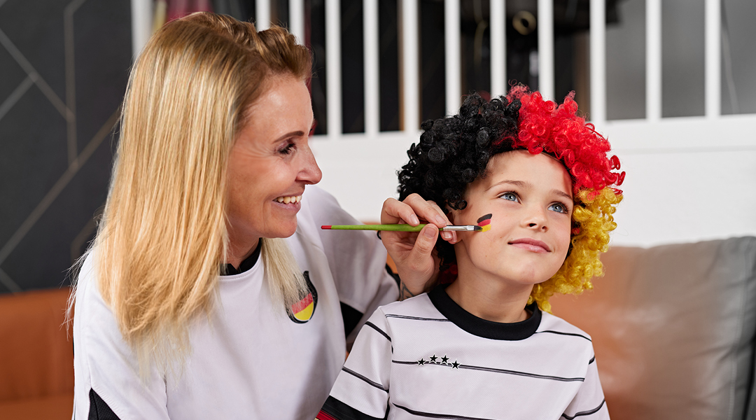 Mutter schminkt Kind eine Deutschlandflagge ins Gesicht